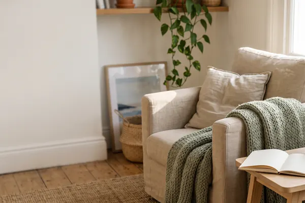 A sunlit corner of a living room with an armchair, a knitted throw and an open notebook